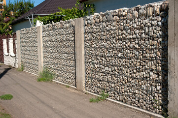 Long-lasting fence without wood and concrete, made of round stone, covered in blocks of stainless steel legs.