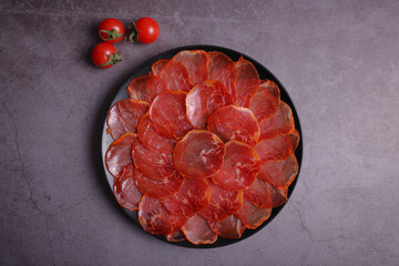 Portion of acorn-fed Iberian loin decorated with cherry tomatoes on a black plate with a dark gray background