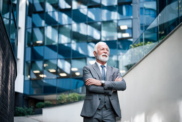 Thoughtful businessman standing with arms crossed against the business office building.