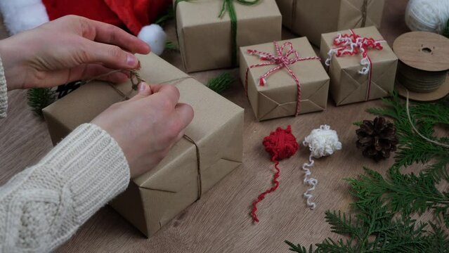 Hands wrap eco friendly presents for Christmas. Plastic-free and sustainable packaging. Recycled paper and twine bow.
