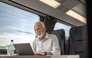 Smiling businessman working on laptop while traveling on passenger train.
