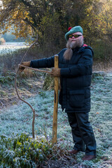 Mann mit langem Bart bindet einen krummen kleinen Baum an einem Stock fest