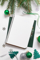 Christmas festive composition with empthy notebook, Christmas green decor, fir tree branches on a green background. Copy space.