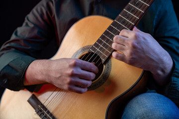 Fototapeta premium The guy in the dark shirt is plucking the strings of a six-string guitar