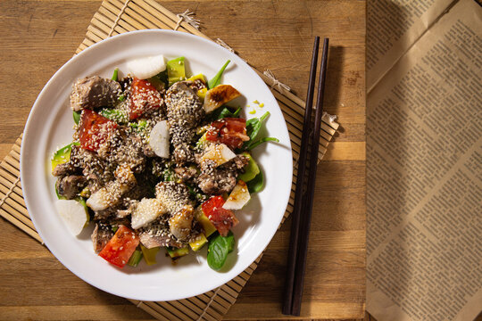 Top View Salad With Tuna And Juicy Vegetables In A White Plate Stands On A Bamboo Makisu And Black Chinese Chopsticks On The Background Of A Wooden Cutting Board And An Old Newspaper