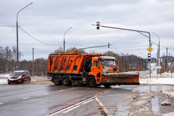 a truck with a bucket transports sand. car sprinkles sand on the road. the fight against ice on the road.