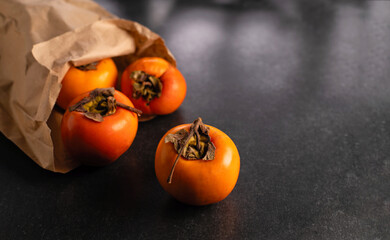 Ripe orange persimmon in wrapping paper, on black stone table, place for text