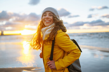 Happy tourist in a yellow jacket posing by the sea at sunset. Travelling, lifestyle, adventure.