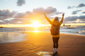 Happy tourist in a yellow jacket posing by the sea at sunset. Travelling, lifestyle, adventure.
