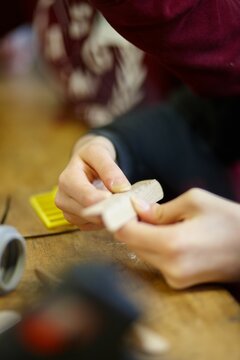 Vertical Closeup Of Hands Making Something From Wood Near Table With Blurred Background