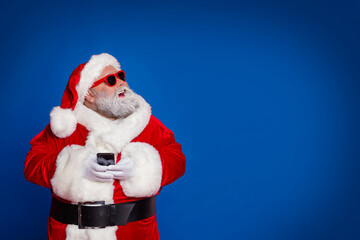 Fototapeta na wymiar Photo of dreamy old man hold telephone look empty space wear santa hat costume isolated red color background