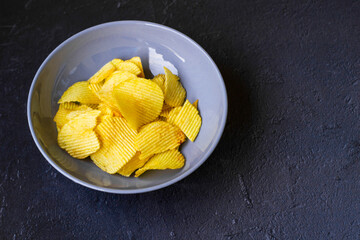 Crispy potato chips in blue bowl on a black slate background