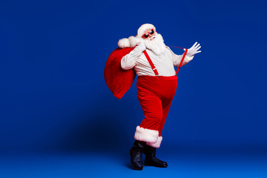 Full length body size view of his he attractive childish cheerful cheery funny fat Santa carrying big large sack having fun dancing isolated bright vivid shine vibrant red color background