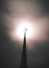 cross on the top of a church steeple backlit by sun in the sky on foggy or wispy cloud sky in background vertical