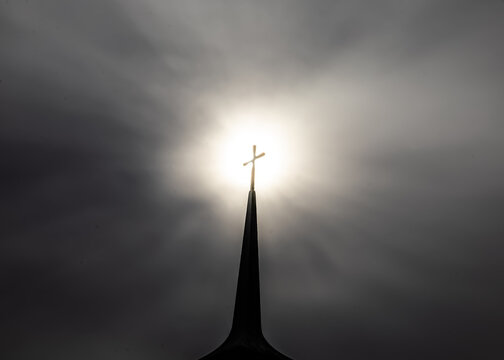 Church Steeple With Cross In The Fog With Sun Setting Behind Backlit