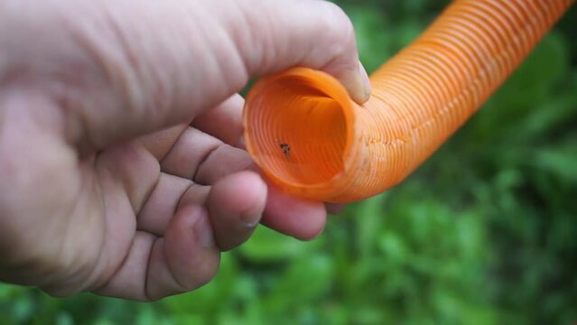 A man's hand holds a yellow jagged plastic hose