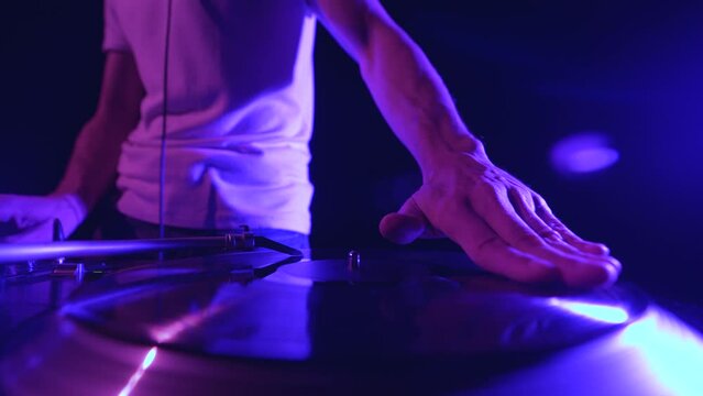 Hip hop dj scratches record on turntables in night club. Club disc jockey scratching vinyl on turn table