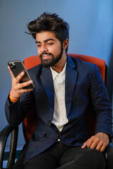 Naklejka premium Businessman sitting on chair isolated. Handsome young indian businessman using mobile phone, confident smile looks. half shot.