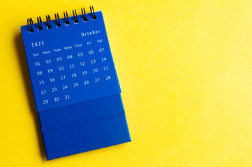 October 2023 blue desk calendar on yellow cover background with customizable space for text.
