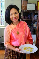 A Thai lady in Thai costume smiles and hold a plate of Thai medicine bolt