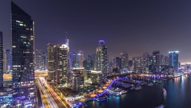 Beautiful aerial skyline day to night transition timelapse of all Dubai Marina promenade and canal with floating yachts and boats after sunset in Dubai, UAE. Modern towers and traffic on the bridge.