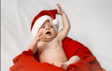 Portrait of a cute beautiful little baby boy wearing red Santa Claus hat on white background with christmas tree toys, traditional Christmas costume. New Year's holidays.