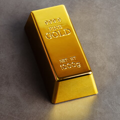 An ingot of gold metal bullion of pure brilliant diagonally located on a gray textured background.