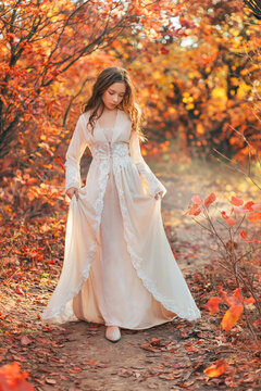 Fantasy portrait teenage princess girl walking in forest path, dirt road. Long blond hair cute face. White vintage dress. Autumn nature red orange leaves trees. Elf nymph young woman. Art photo image