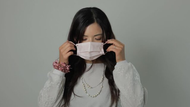 Asian young woman put a mask on reluctantly. Unhappy, Tired, Disappointed. White background.