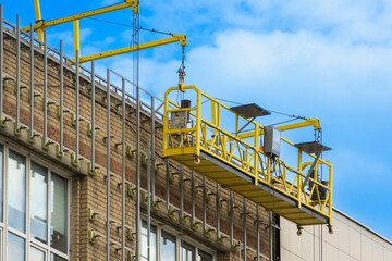 Construction hoist on the facade of the building. House cladding work. Empty facade elevator on cables.