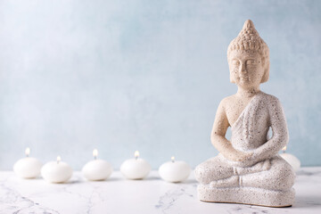 Statue of Buddha and burning small white candles against blue textured wall. Wellbeing spa time concept. Place for text.
