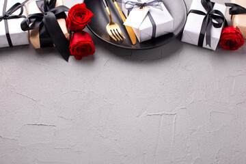 Romantic layout.  Black plate, knife, fork, boxes with presents and red roses flowers on textured...