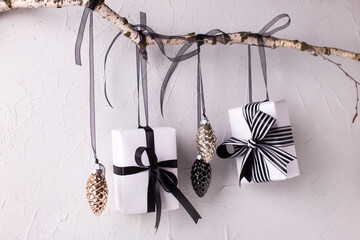 Wrapped black and white boxes with presents and decorative cones hanging on a branch against...
