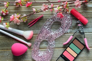 Pink-themed makeup flatlay on wood background