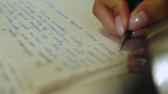 Female hands write letter on white paper on wooden table. Wedding preparations. Bride vow to groom. Loving words. Beautiful manicure.Close-up.