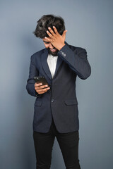 Portrait of a handsome happy young businessman wearing suit standing isolated over gray background, using mobile phone, video call concept