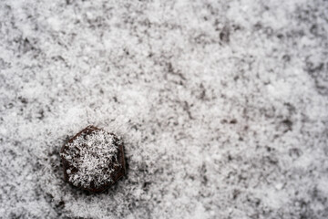 Minimalistic abstract winter pattern, crystals of white snowflakes on a black metal hat on a blurry white background of snow, resistance to frost and hardships, geometric winter pattern. Flatlay