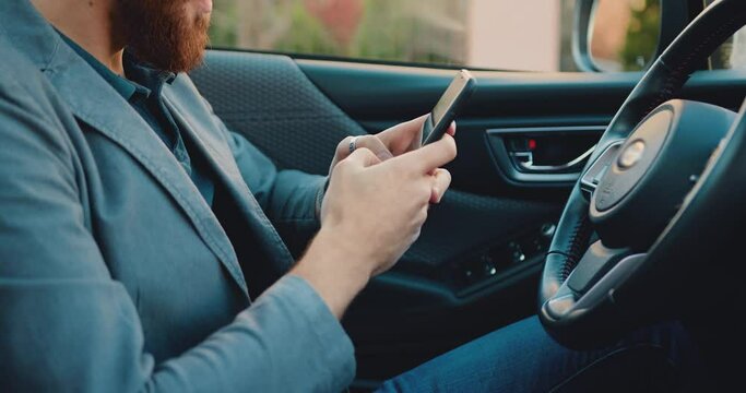 Close-up businessman using and typing smartphone, in car handheld shot. Technology concept. Unknown male professional chatting using phone at car.