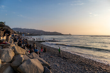 People enjoying on the rocky shores, beautiful sunset and incredible waves of Barranco beach in Lima, Peru.