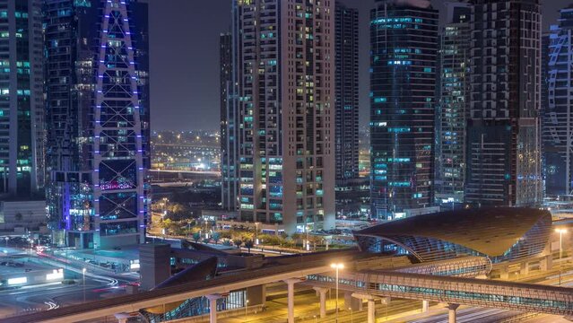 Aerial view of Jumeirah lakes towers skyscrapers day to night transition timelapse with traffic on sheikh zayed road and metro line with footbridge