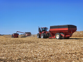 combine harvesting a corn field and loading a grain cart while a 2nd tractor and grain cart waits...