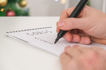 Man writes marker board at white table with Christmas decor goals and plans new year and Christmas. Goals New Year and Christmas written marker board. List wishes and goals new year and Christmas 2023