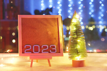 The numbers new year 2023 on a beautiful easel next to Christmas tree and lamp. Discounts,...