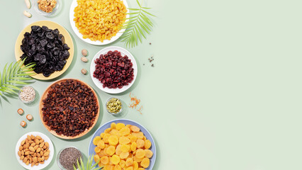Natural dry fruits, nuts and seeds assortment on a blue background with palm leaves and copy space. Healthy snack - mix of organic nuts and dry fruits. Vegan and vegetarian products. Flat lay