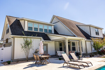 The side view of a long craftsman cottage white cream new construction house with a covered patio...