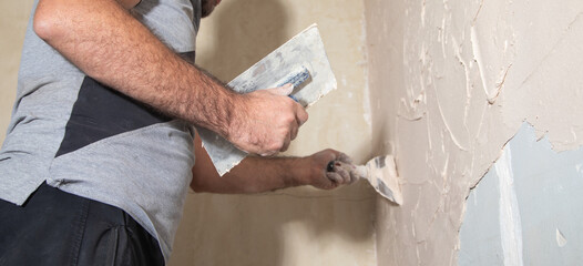 Man is applying putty on a wall. Renovating house