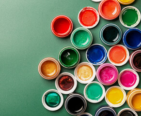 Bright, mother-of-pearl, multicolored open cans of paint on a green background. View from above.
