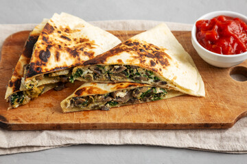 Homemade Spinach and Mushroom Quesadilla with Salsa on a rustic wooden board, low angle view