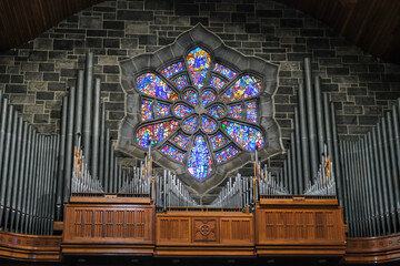 Pipe organ in a cathedral with colorful stained glass in the background.
