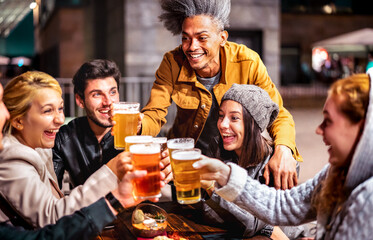 Happy friends drinking beer at brewery bar garden out door - Multiracial life style concept with genuine people enjoying time together eating at restaurant patio - Vivid filter with focus on mid guy